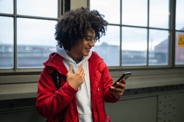 Curly-haired young guy in red jacket with a phone in hands