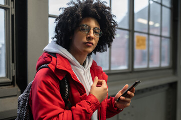 Curly-haired young guy in red jacket with a phone in hands