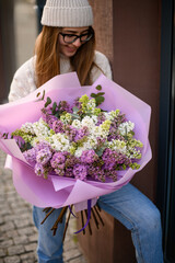 Look down girl in warm knitted hat with a chic bouquet of lilac bushes - 791926401