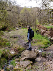 Young photographer standing on a large rock in a forest woodland scene with a slow moving moorland stream surrounded by trees