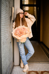 Beautiful girl in beige sports shoes standing near a wall with a chic roses - 791927469