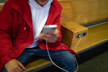 Close up picture of a guy with phone in hands sitting on the bench