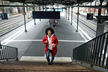 Curly-haired young guy in red jacket at the railway station