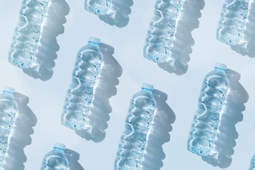 Minimal Pattern Plastic bottles water at sunlight with shadow on blue, aesthetic top view. Distilled drinking water. Pollution, environmental protection. Eco trend to reduce disposable plastics