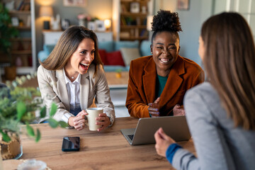 Group of female colleagues using laptop and smiling.