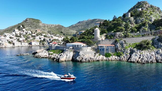 Aerial drone cinematic video of water taxi cruising near picturesque and historic main village of Hydra or Ydra island well know for captain's mansions and marine tradition, Saronic gulf, Greece