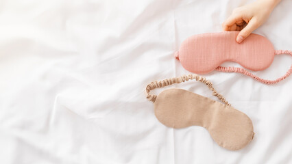 Eye masks for sleep pink and beige color in woman hand on white bedclothes, minimal lifestyle...
