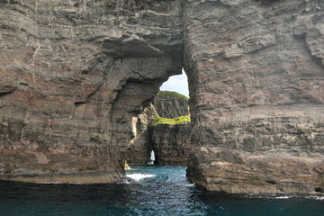 Rocks and caves of the coast near the famous spireTrøllkonufingur  towering rock formation on...