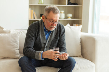 Middle aged senior man holding medical pill and glass of water. Mature old senior grandfather...