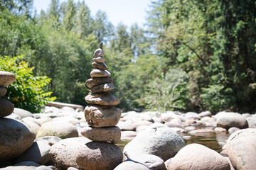 Fototapeta na wymiar Rock pile or rock stack in front of defocused forest on a sunny day. Pebble tower or rock pyramid. Concept for relaxing, zen, spiritual or yoga. Nature background. Selective focus. North Vancouver BC