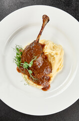 Classic dish french cuisine - roasted duck leg in sauce with garnish on black background. Cooked...