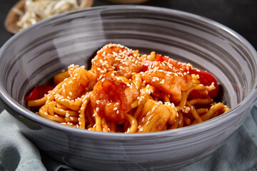 Handmade wheat noodles with shrimps and vegetables in sweet chili sauce, on a black background with...