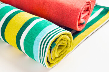 Large size, two colorful beach towels rolled on white surface