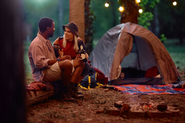 Young couple drinking beer and talking while camping in forest.