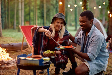 Young happy couple of campers grilling food in nature.