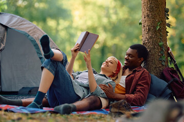 Happy couple of campers reading book in forest.