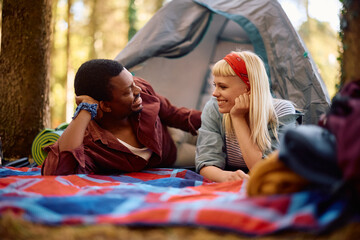 Young happy couple talking while relaxing by  tent on camping.