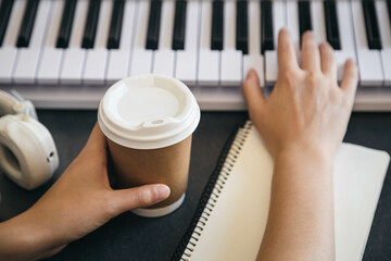 A cup of coffee in the hands of a female keyboard player at the workplace.