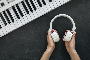 White headphones in female hands and a piano on a textured black background.
