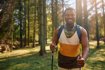 Happy black man enjoying in hiking in forest and looking at camera.