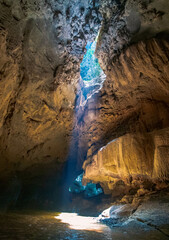 The sun is shining on stalactites and stalmites at the top of the cave. In the cave in Trang, Thailand, there is a small canal.