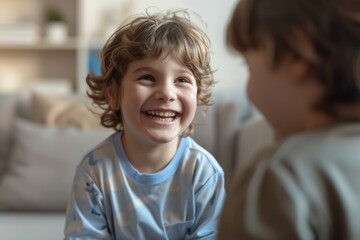 A cheerful young boy with curly hair is happily smiling at someone, likely a friend or family member, indoors