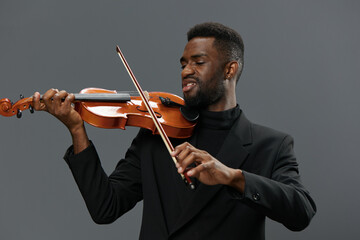 African American man in elegant black suit playing violin against gray background, music...