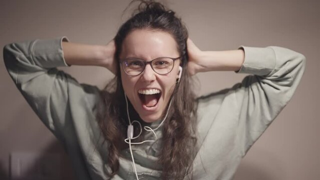 Excited woman with long curly hair and glasses dancing crazy laughing and yelling into her earbuds, enjoying herself on favour music