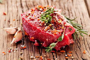 Raw beef steaks with herbs and spices ready for cooking are on wooden board.