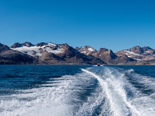 Boat trip on the Sangmileq Fjord towards the Ikaasatsivaq Fjord in East Greenland. In the background a red boat for a mighty mountain range.