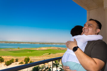 a man holds a little girl in his arms on a balcony against the backdrop of a golf course and the...