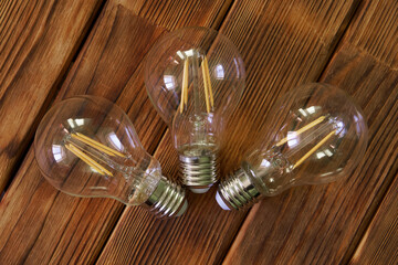 Three clear LED filament lamps with yellow filaments on natural pine boards. Eco-friendly energy. Photo. Copy space