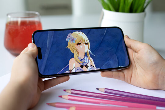 Children hands holding iPhone 15 Pro Max with game Genshin