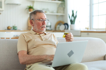 Senior man shopping online using laptop paying with credit card. Old grandfather buying on Internet...