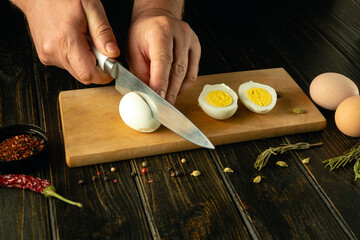 A cook cuts a boiled egg with a knife before preparing an eggs dish. Low key calorie diet concept...