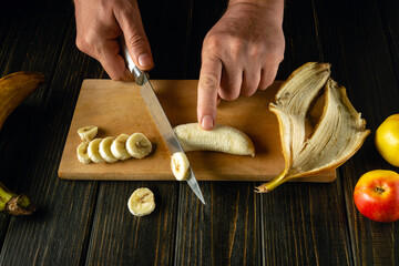 Chefs cutting banana on a wooden boards. Low key concept of preparing a fruity breakfast dish on...