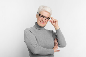 Smiling senior woman with glasses on grey background