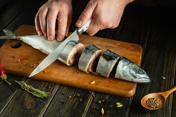 The chef cuts raw fish with a knife before salting it. Spices on the kitchen table for preparing a...