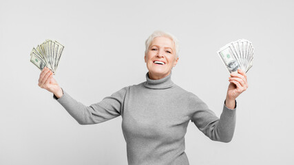 Senior joyously showing off her money on grey background