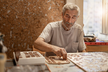 gray-haired   senior man playing  jigsaw puzzle as dementia therapy