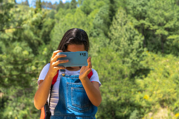 Frontal shot of a young traveler taking pictures with her cell phone outdoors, mountain scenery.
