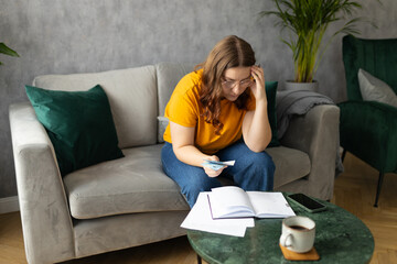 The 30s woman considers the costs of gas, electricity, heating. The concept of increasing tariffs for services. Woman with financial bills calculating on smart phone. Debt, bankruptcy