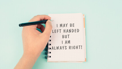 I may be left handed but I am right is standing on a notebook, writing with the left hand, pen and table