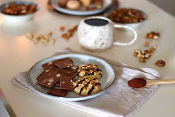 Cup of tea or coffee, cookies, macaroons, chocolate, various nuts and cocoa powder on white background. Selective focus.