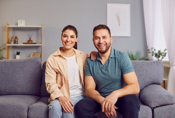 Portrait of a young, happy, smiling family couple sitting together on a sofa at home. Married...