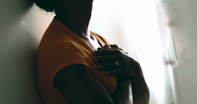 One spiritual young black woman putting hands on chest feeling GRATITUDE. Earnest African American person feeling heartfelt contemplation leaning on wall