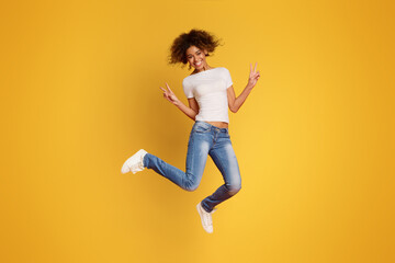 African-american joyful lady jumping and gesturing peace