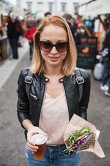 Beautiful young woman holding delicious organic salmon vegetarian burger and homebrewed IPA beer on open air beer an burger urban street food festival in Ljubljana, Slovenia