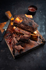 Traditional barbecue burnt chuck beef ribs marinated with spicy rub and served as close-up on an old rustic wooden board with knife