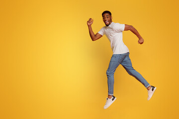 Excited african-american man jumping on orange background